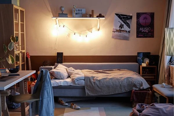 A cozy bedroom with a neatly made bed, warm lighting, musical instruments, and posters on the wall.