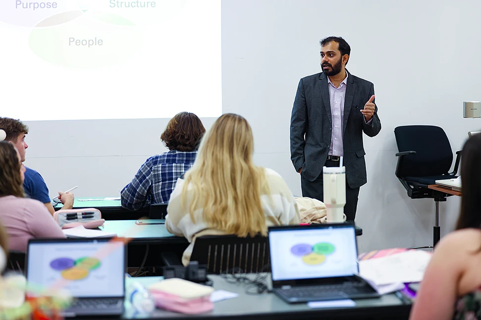A man is giving a presentation to a group of seated individuals, with a projected slide displaying a Venn diagram in the background.